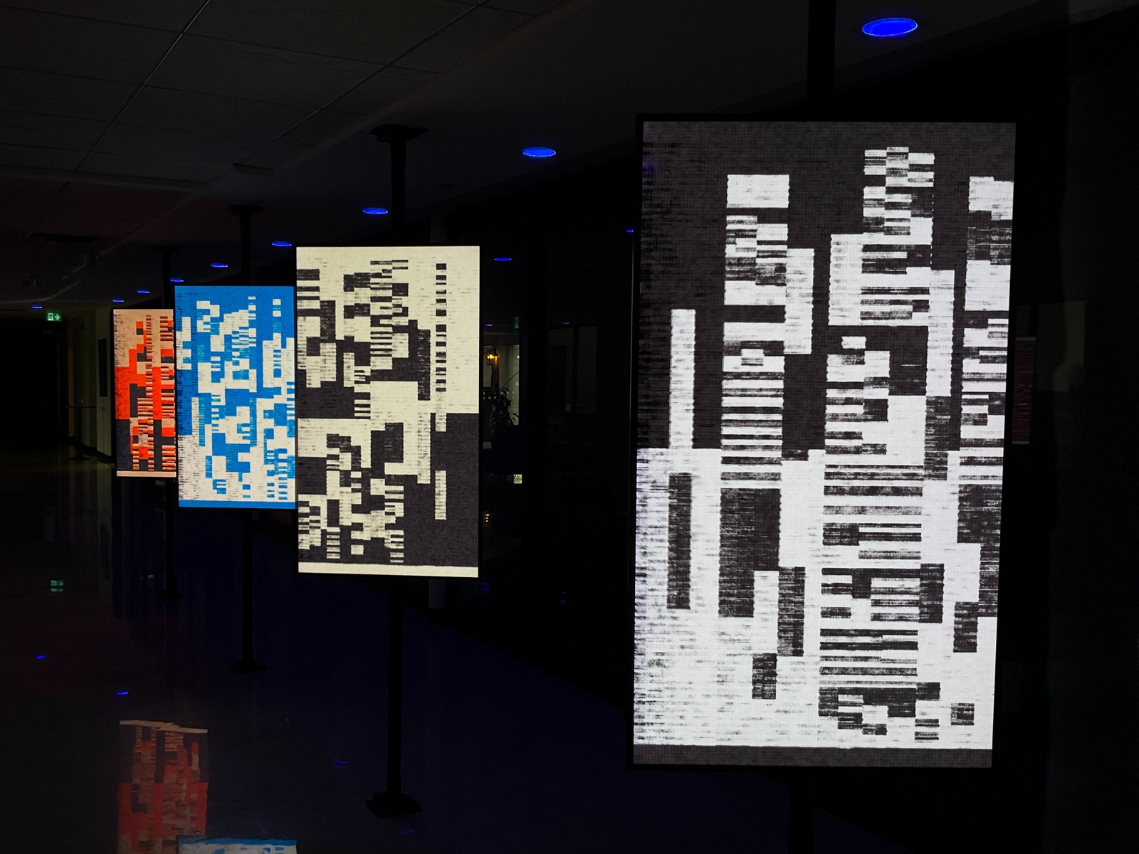 A side view of the Montreal exhibition, showing black and cream, blue and orange works across a row of screens