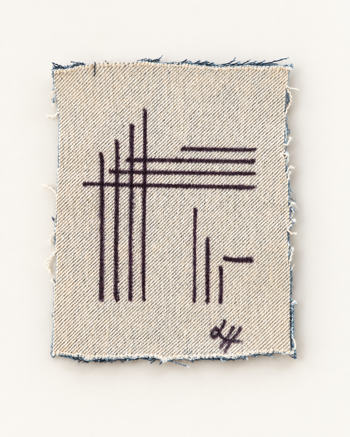 Fine black lines intersect across a small cream denim fragment with frayed edges.
